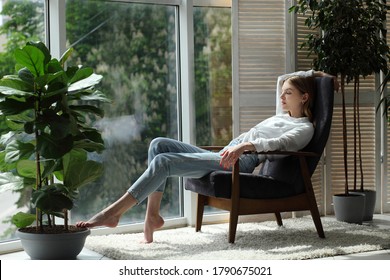 Young Woman At Home Sitting On Modern Chair Near Window Relaxing In Living Room