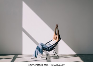 Young Woman At Home Sitting On Modern Chair Relaxing In Her Living Room