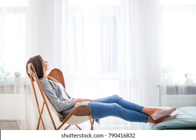 Young woman at home sitting on modern chair near window relaxing in living room - Shutterstock ID 790416832