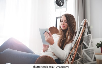Young woman at home sitting on modern chair and using tablet computer, relaxing in living room - Shutterstock ID 791218393