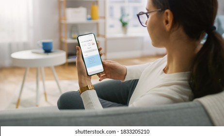 Young Woman at Home Uses Smartphone for Checking Weather Predictions and Coming Day Plans in Daily Schedule Calendar. She's Sitting On a Couch in Her Cozy Living Room. Over the Shoulder Shot - Shutterstock ID 1833205210
