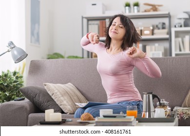 Young woman at home waking up after a bad night's sleep on the couch, she's stretching