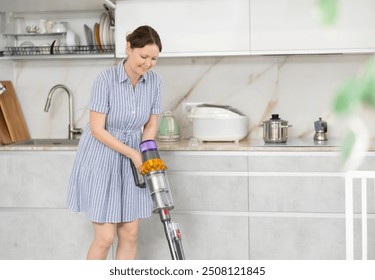 Young woman in homemade blue dress doing household chores. Experienced housewife with vacuum cleaner furbish cleanse carpeting synthetic covering near dining table in kitchen - Powered by Shutterstock