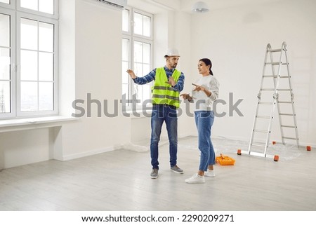 Young woman homeowner discussing design project or repair of her new apartment with foreman standing in empty white room. Meeting with builder about interior decoration or home layout. Moving concept.