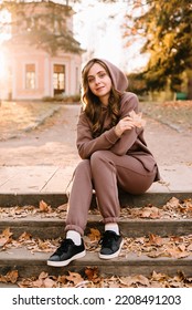 Young Woman In Hoodie Sitting On The Steps In An Autumn Park. Sunny Weather. Fall Season.