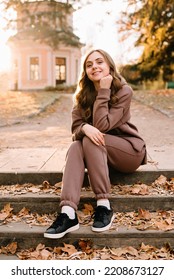 Young Woman In Hoodie Sitting On The Steps In An Autumn Park. Sunny Weather. Fall Season.