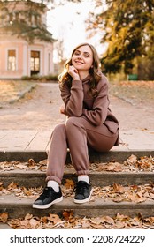 Young Woman In Hoodie Sitting On The Steps In An Autumn Park. Sunny Weather. Fall Season.