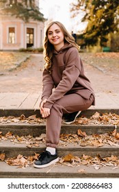 Young Woman In Hoodie Sitting On The Steps In An Autumn Park. Sunny Weather. Fall Season.