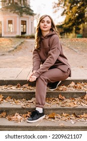 Young Woman In Hoodie Sitting On The Steps In An Autumn Park. Sunny Weather. Fall Season.