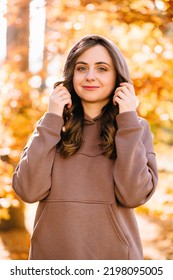 Young Woman In Hoodie Spends Time In An Autumn Park. Sunny Weather. Fall Season.