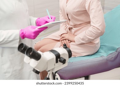 A young woman in a hospital gown at a gynecologist's appointment. A gynecologist wearing pink gloves writes a prescription to a patient. Woman on gynecological chair closeup unrecognizable colposcopy - Powered by Shutterstock