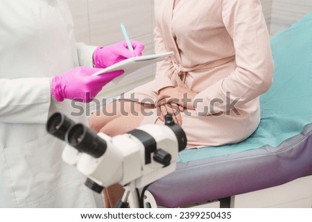 A young woman in a hospital gown at a gynecologist's appointment. A gynecologist wearing pink gloves writes a prescription to a patient. Woman on gynecological chair closeup unrecognizable colposcopy