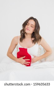 Young Woman With Hot Water Bottle On Stomach Sitting In Bed