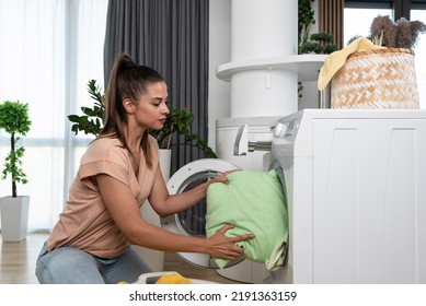 Young woman or housewife putting clothes and laundry to the washing machine to wash the stuff to be clean and fresh. Girl work as a maid to pay her college bills washing laundry. - Shutterstock ID 2191363159