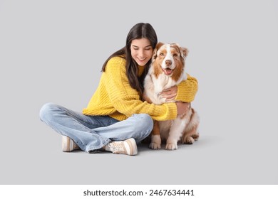 Young woman hugging Australian Shepherd dog on light background - Powered by Shutterstock