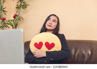 A young woman hugging an emoji stuffed toy, thinking about her love ones, motivating her to work harder.