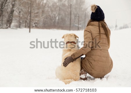 Young woman hugging her dog in the snow while both are looking away from the camera