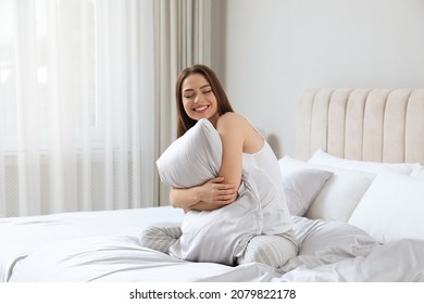 Young woman hugging pillow on comfortable bed with silky linens