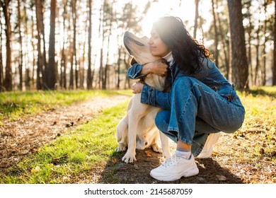 A Young Woman Hugs Her Beloved Dog. Girl And Labrador In The Spring Forest At Sunset