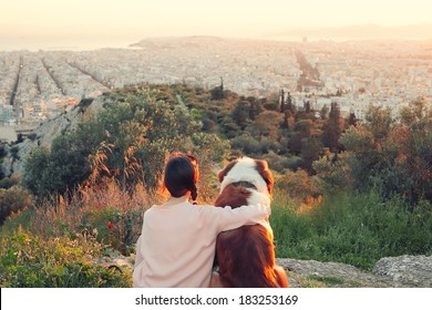 Young Woman Hugs Her Dog As They Sit In A Field.Athens,Greece.Real Warm Light From Sunset.