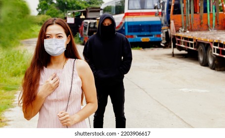 Young woman hygienic mask walks alone being careful to protect herself when she learns that she is being driven by a black robed man walking behind him to rob valuables : Crime concept
 - Shutterstock ID 2203906617