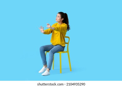 Young Woman With Imaginary Steering Wheel Sitting In Chair On Color Background