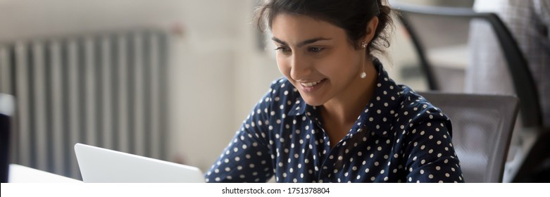 Young woman Indian employee sit at desk in office room use computer do work. Workday, human resources, career, new app corporate program usage concept horizontal photo banner for website header design