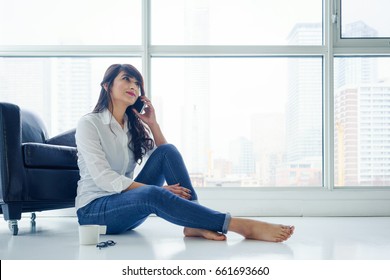 Young woman indoors, sitting on floor next to window using mobile phone. young adult arabic pretty 20 years old