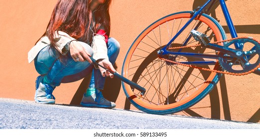 Young Woman Inflating Bike Wheel In A Sunny Day Outdoors - Girl Fixing Bicycle Tire Outside At Summer Time Coming On Orange Urban Wall Background - Concept About Two Wheeler Commuter Lifestyle 