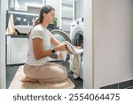 Young woman Inserting clothes inside the washing machine In home bathroom. High quality photo