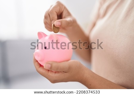 Young woman inserting coin on piggy bank at home