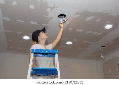 A Young Woman Installing A Ceiling Light For  DIY Kitchen Remodel.