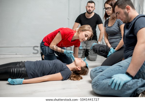 Young woman instructor\
showing how to lay down a woman during the first medical aid\
training indoors