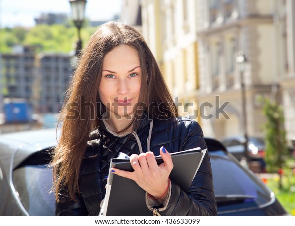 Young woman insurance agent or sales agent prepares
documents outdoors on city background. Business woman with folder
of documents in her hands outdoors. Woman conducting a survey and
writing data.