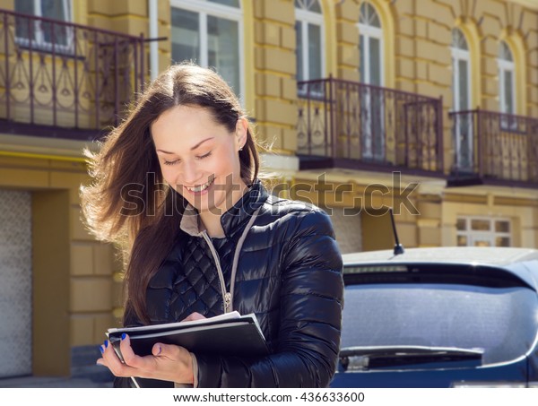 Young woman insurance agent or sales agent prepares\
documents outdoors on city background. Business woman with folder\
of documents in her hands outdoors. Woman conducting a survey and\
writing data.