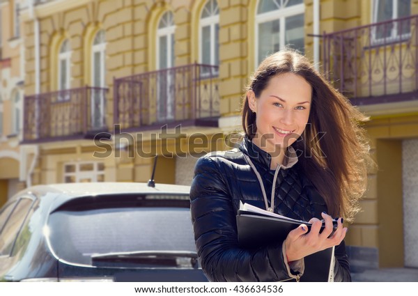 Young woman insurance agent or sales agent prepares\
documents outdoors on city background. Business woman with folder\
of documents in her hands outdoors. Woman conducting a survey and\
writing data.