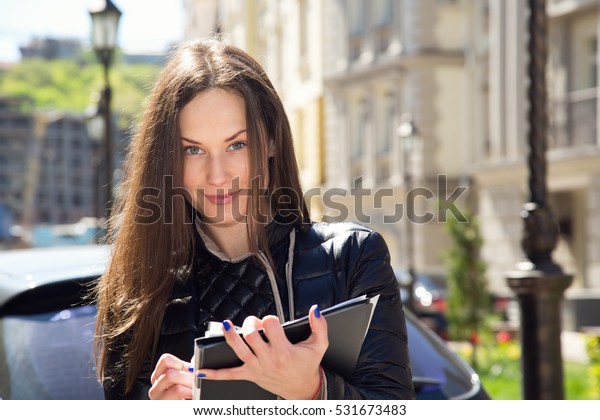 Young woman insurance agent or sales agent prepares\
documents outdoors on city background. Conducting social survey and\
writing data.