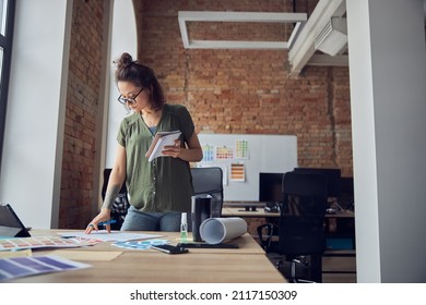 Young Woman, Interior Designer Or Architect In Casual Wear With Messy Hairdo Making Notes On A Blueprint, Working On New Project, Standing In Her Office