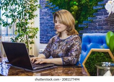 A young woman interior designer is working in her office at a computer. Green office, live plants in an office space, a wall made of stabilized moss, epoxy resin table