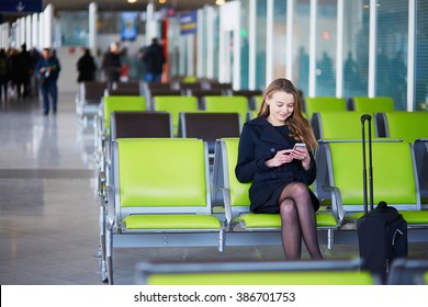 Young Woman In International Airport, Checking Her Phone While Waiting For Her Flight