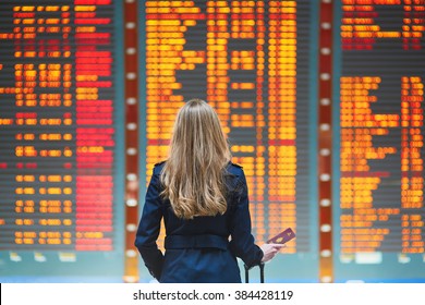 Young woman in international airport looking at the flight information board, checking her flight - Shutterstock ID 384428119