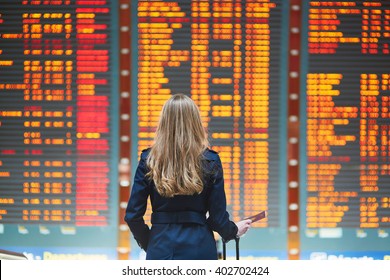 Young woman in international airport looking at the flight information board, holding passport in her hand, checking her flight - Shutterstock ID 402702424