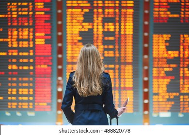 Young woman in international airport looking at the flight information board, holding passport in her hand, checking her flight - Shutterstock ID 488820778