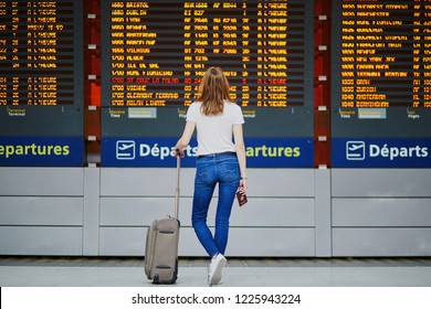 Young Woman In International Airport With Luggage And Passport Near Flight Information Display