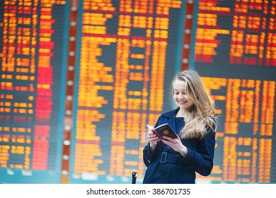 Young woman in international airport near the flight information board, checking her passport - Shutterstock ID 386701735