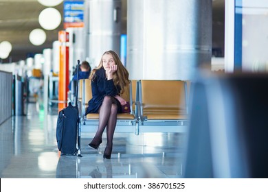 Young woman in international airport, waiting for her flight, looking upset or worried. Missed, canceled or delayed flight concept