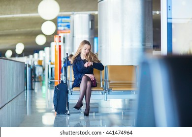 Young woman in international airport, waiting for her flight, checking her watch and looking upset or worried. Missed, canceled or delayed flight concept