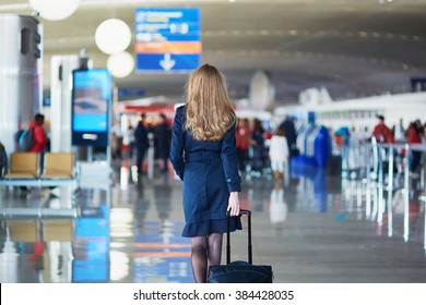 Young Woman In International Airport, Walking With Her Luggage, Back View. Flight Attendant Going To Meet Her Crew