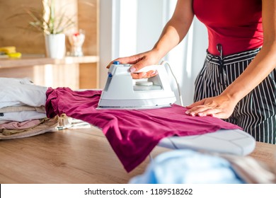 Young woman ironing clothes. Close up hand of woman ironing clothes on the table. Closeup of woman ironing clothes on ironing board. Household duties, taking care of clothes concept. 
