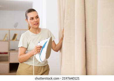 Young Woman Ironing Curtains At Home